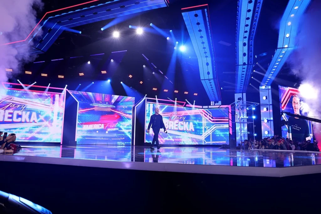 Gary Brecka walking onto a large stage with bright lights and digital screens at a live speaking event.