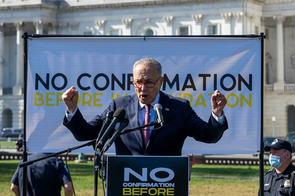 Chuck Schumer speaking at a Senate press conference in front of a Supreme Court confirmation banner.