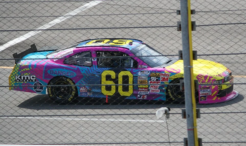 Travis Pastrana's pink and blue number 60 Roush Fenway Racing stock car on a NASCAR track