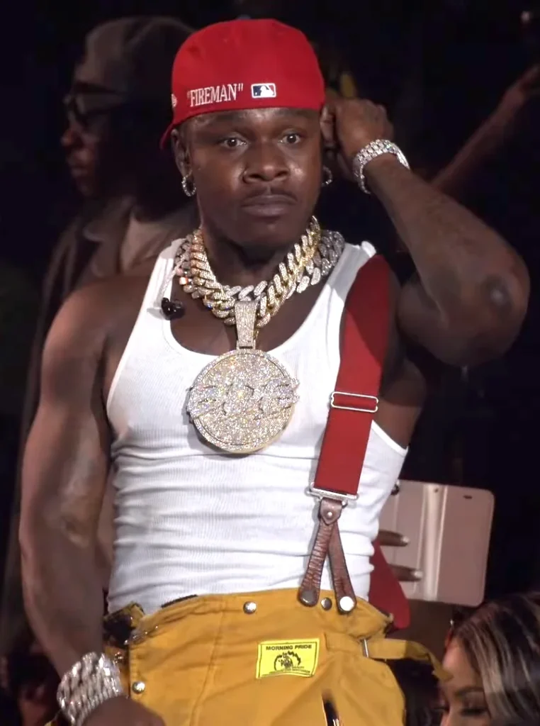 Rapper DaBaby performing live on stage in diamond jewelry and a red hat.
