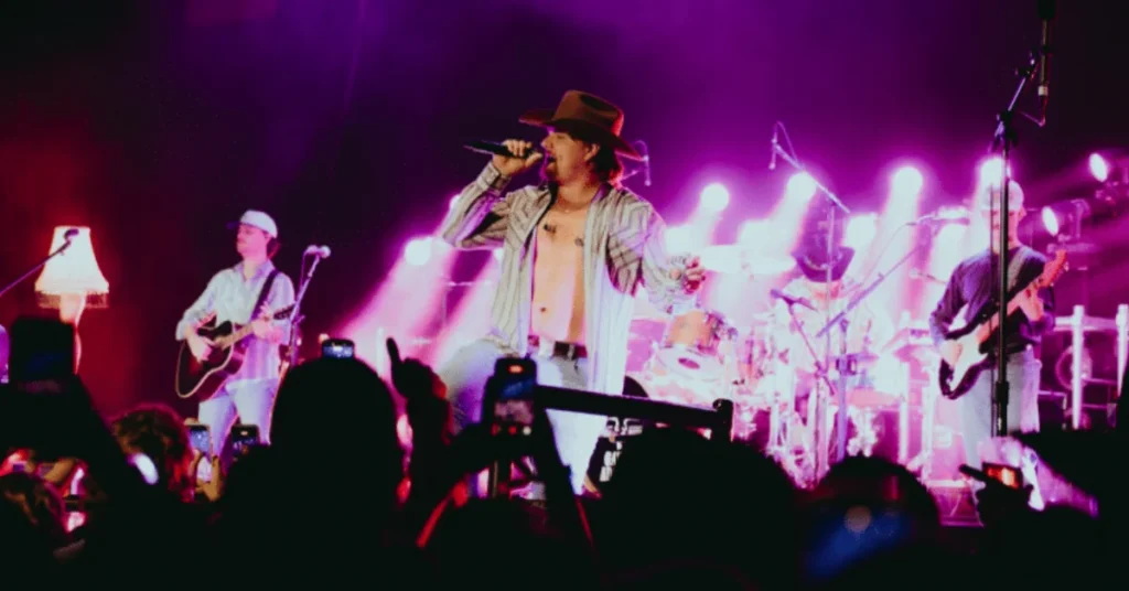 Country music artist Gavin Adcock singing live on stage with his band in front of a large concert crowd with purple stage lights.