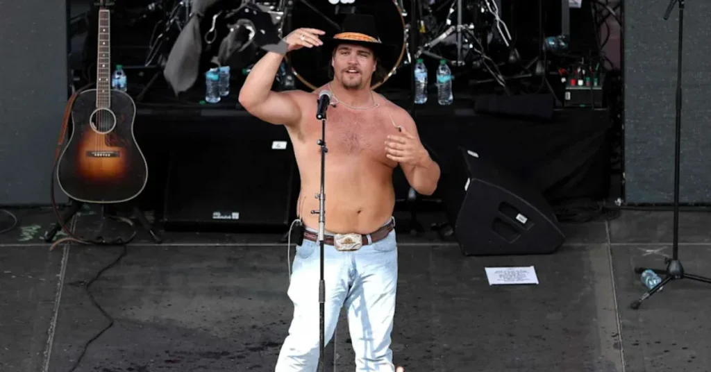 Shirtless country music artist Gavin Adcock performing live on stage in a black cowboy hat and jeans.
