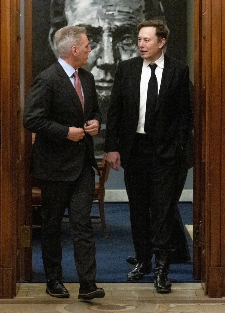 Elon Musk walking and conversing with Kevin McCarthy in a doorway at the U.S. Capitol building.