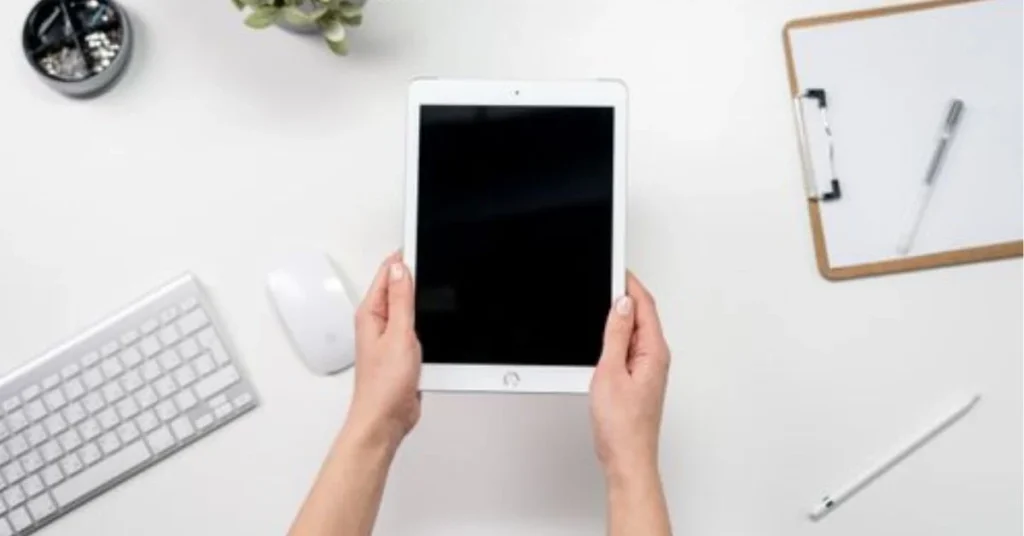 Hands holding iPad on clean white desk with keyboard and Apple Pencil beside it